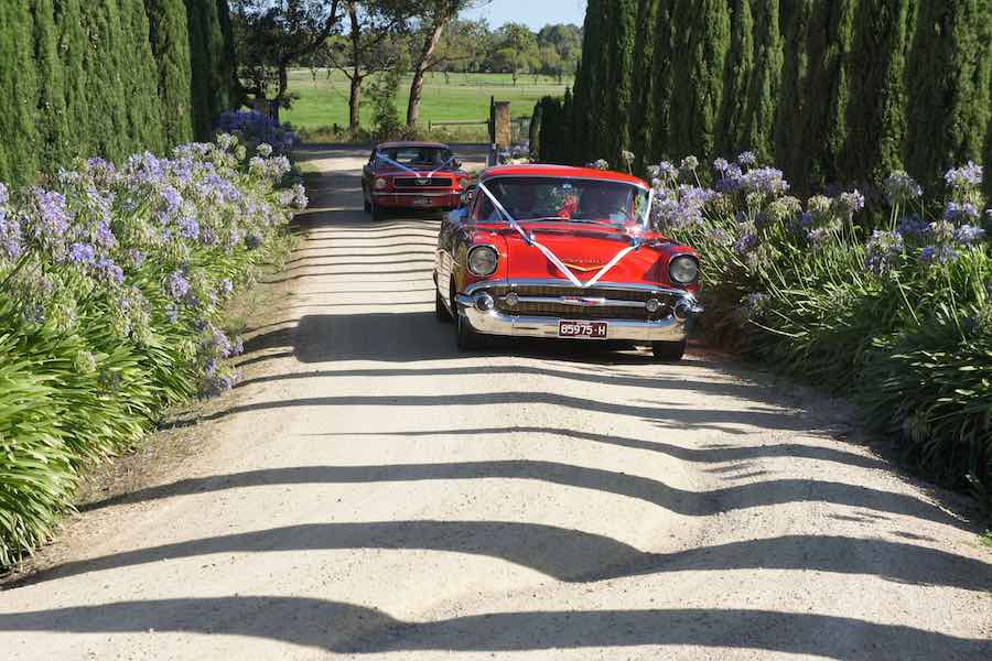 2 classic red cars arriving at a wedding ceremony