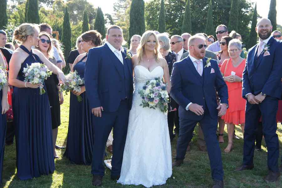 Bride, Groom, Family & Friends pose for a photographer at an outdoor wedding ceremony